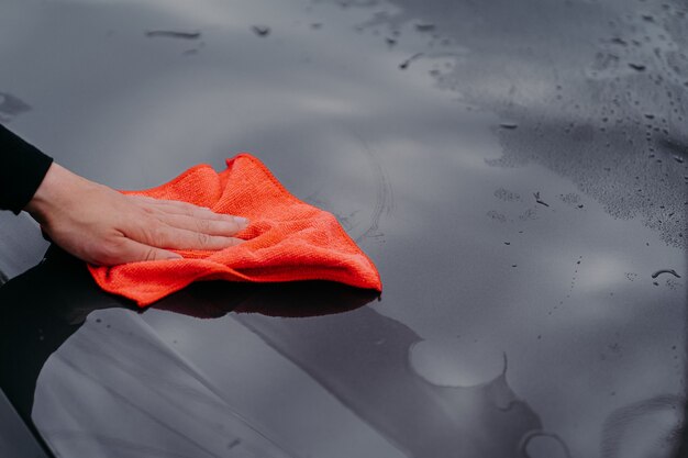 Man cleans the surface of car with microfiber cloth