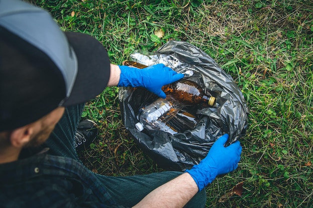 Foto un uomo ripulisce la foresta getta una bottiglia in un primo piano del sacco della spazzatura