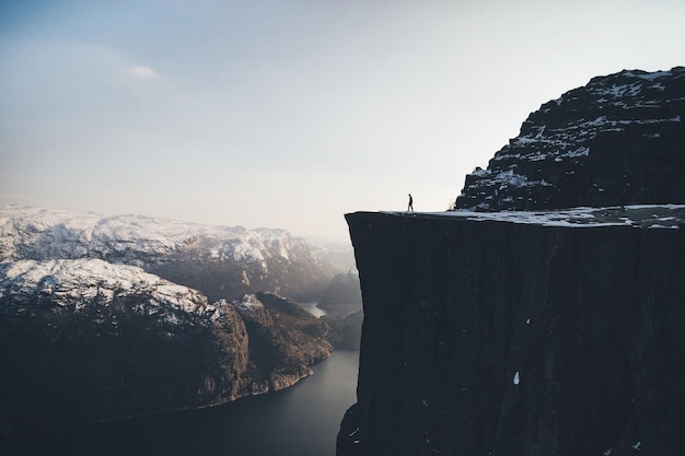 Photo man on cliff by river against sky during winter