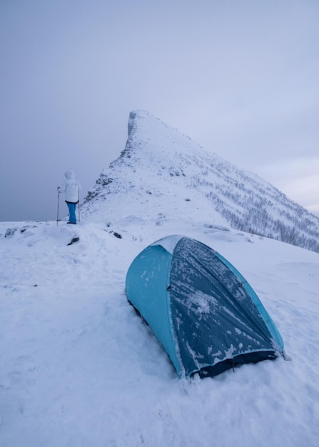 Uomo scalatore con tenda da campeggio sul picco di montagna di neve in cupo