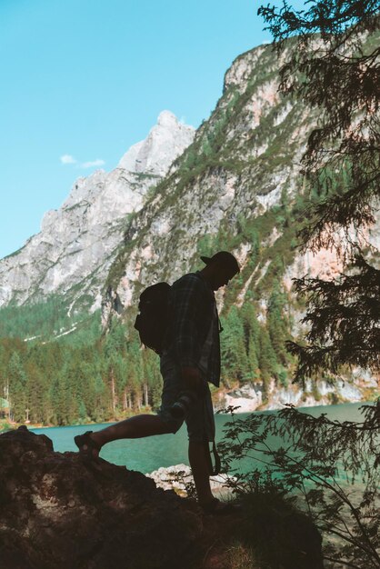 Uomo che si arrampica sulle rocce per riprendere il bellissimo paesaggio del lago e delle montagne. attività di fotografo