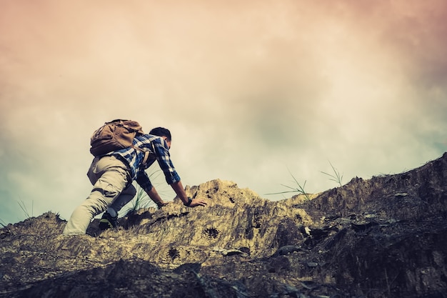 男勝利を見つけるためにオレンジの空の背景の下に山を登る/登山者