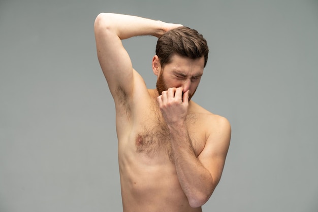 Photo man closed his nose while sniffing his armpit over the grey background hygiene concept stock photo