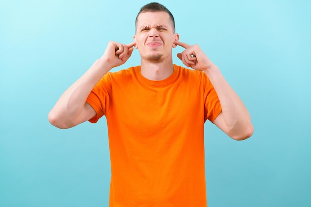 A man closes his ears and squints his face at a blue background\
too loud frustrated expression guy headache loud pensive solution\
failure deaf office caucasian face portrait anger