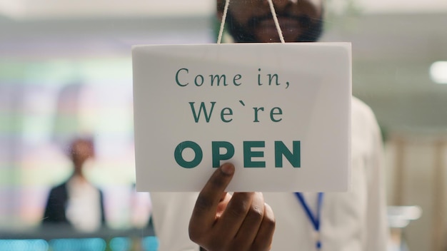 Photo man closing clothing store at night after selling entire merchandise stock retail assistant turning opened message sign on fashion boutique door in mall department extreme close up shot