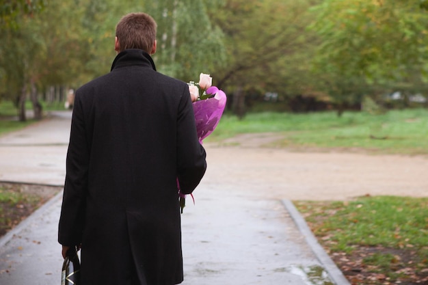 A man in a coat with flowers and wine in the Park. The view from the back. Is