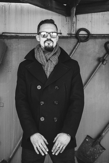 A man in a coat with a scarf poses on the street to advertise men's clothing.