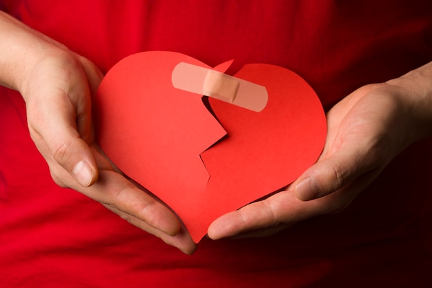 Un uomo raccoglie un cuore rosso spezzato tra le mani. concetto di amore e relazioni.