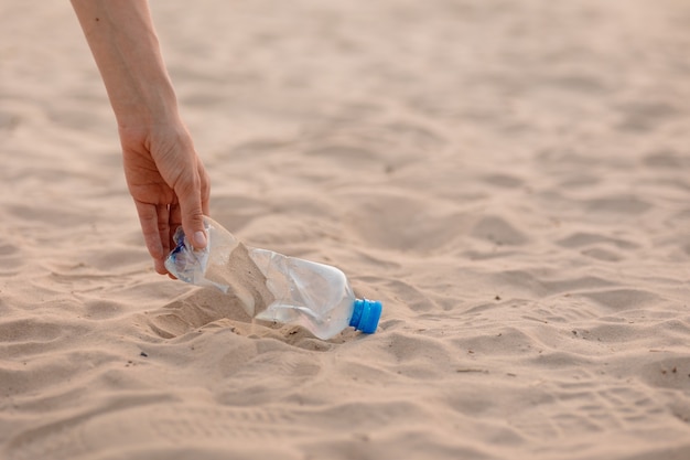 Un uomo raccoglie bottiglie di plastica e spazzatura sulla spiaggia in un luogo pubblico ecologico e attento