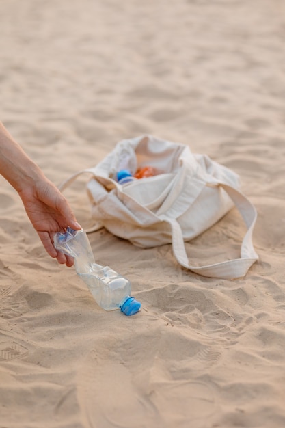 한 남자가 친환경적이고 돌보는 공공 장소에서 해변에서 플라스틱 병과 쓰레기를 수집합니다.