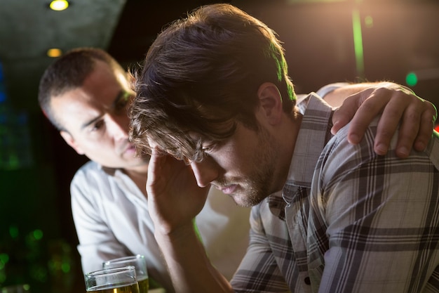 Человек утешает своего подавленного друга в баре