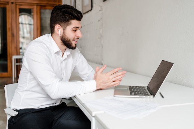 Man communicating on laptop with wireless earpods in the office