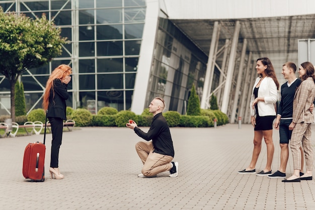 A man in the company of friends meets his girlfriend with luggage at the airport makes an offer to a red-haired girl