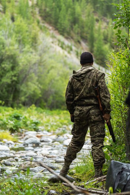 A man in a comuffle with a rifle in his hands looks forward. Duck hunting.