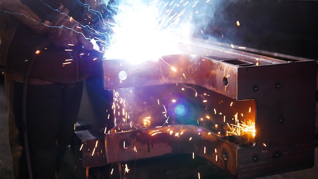 A man at the construction plant using a welding machine Bright blue lighting Sparkles falling on the ground