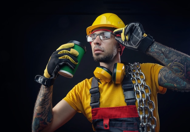 A man in a construction repairman's jumpsuit with a metal chain drinks a drink