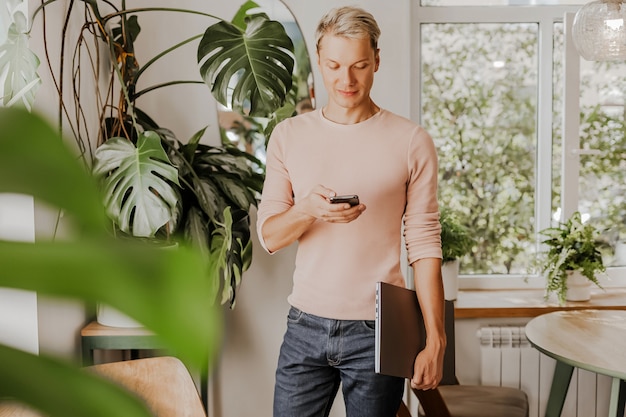 Man controleert de telefoon, zakenman met laptop in werkruimte in eco café met planten