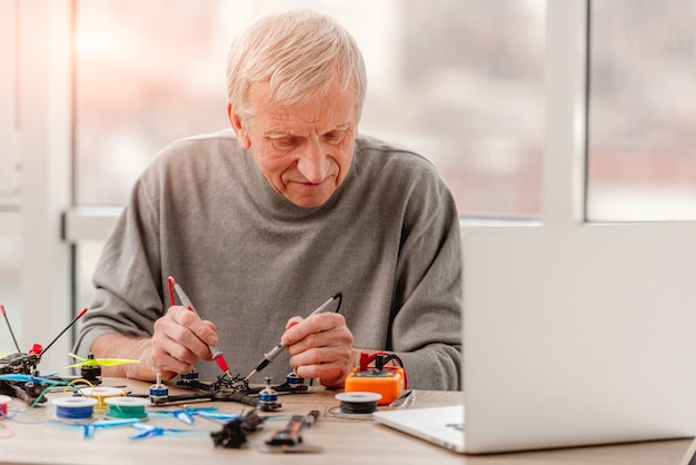 Man controleren opladen zitten bij de tafel met tools en laptop tijdens het reparatieproces van de quadcopter