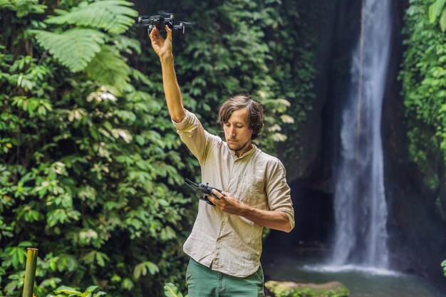Мужчина управляет дроном на фоне леса и водопада