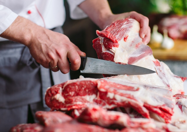 A man cook cuts meat with a knife in a restaurant.