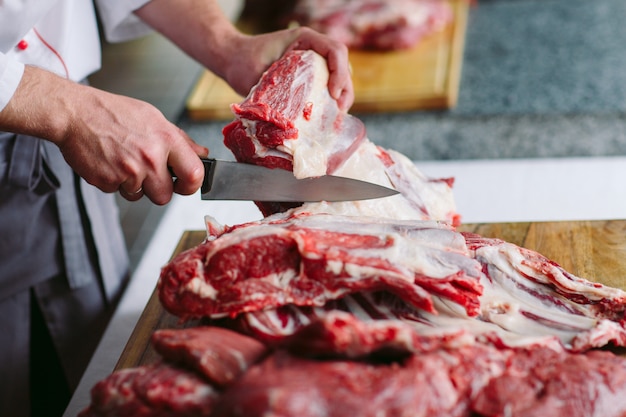 A man cook cuts meat with a knife in a restaurant.