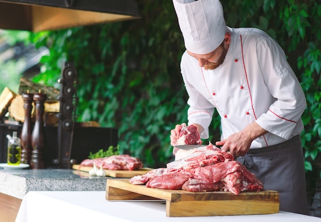 A man cook cuts meat with a knife in a restaurant.