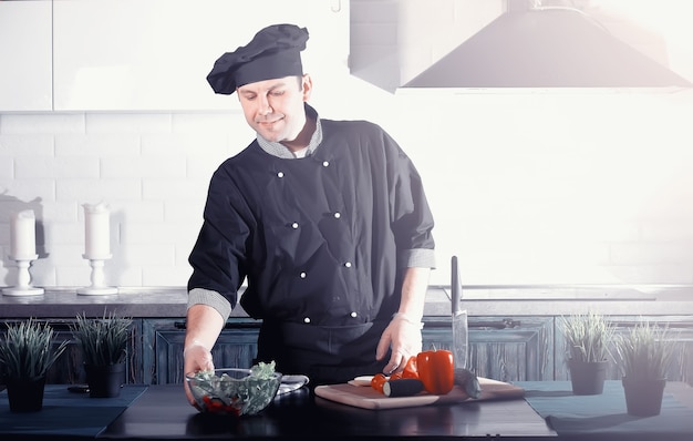 Cuoco dell'uomo che prepara il cibo al tavolo della cucina di verdure