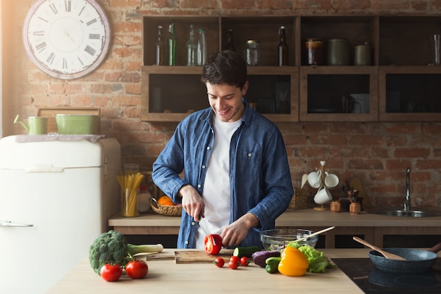 Man cooking delicious and healthy food in the loft kitchen at home on sunny day. Preparing vegetable salad.