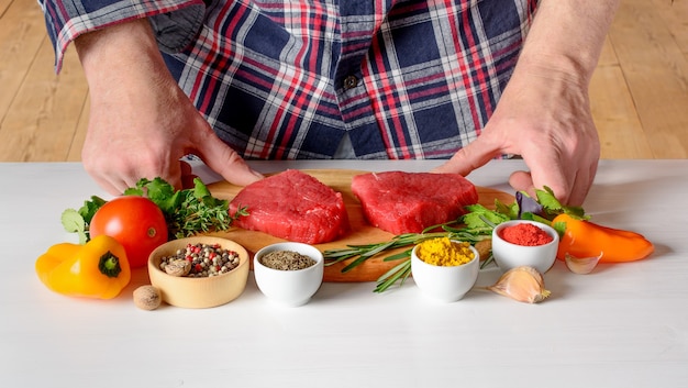 Uomo che cucina bistecche di filetto mignon con spezie erbe e verdure sulla cucina di casa