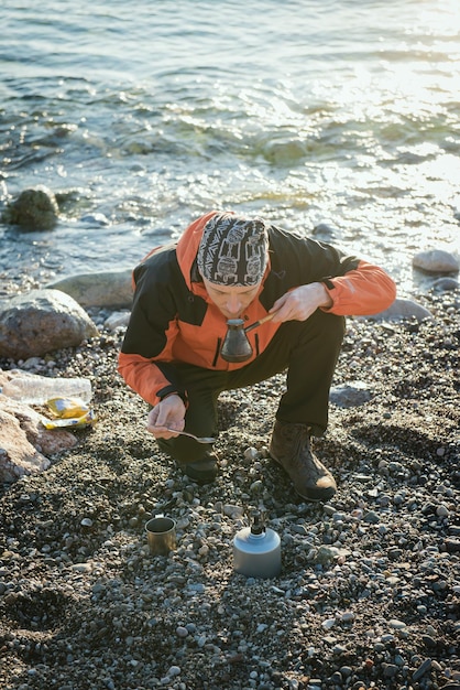 Photo man cooking fresh morning coffee near the sea on torch fire. traveling with taste. fresh aroma of coffee outdoors while traveling.