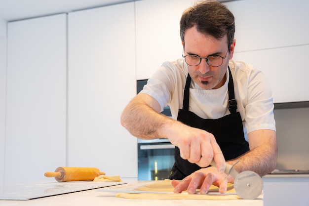 Man cooking homemade croissants measuring puff pastry and making cuts work at home