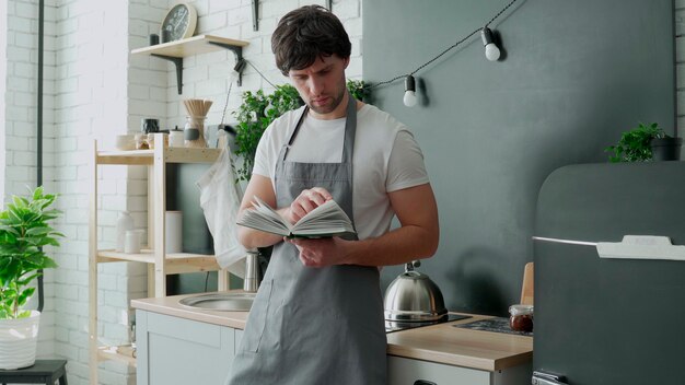 料理本からレシピを読んでキッチンで料理する男