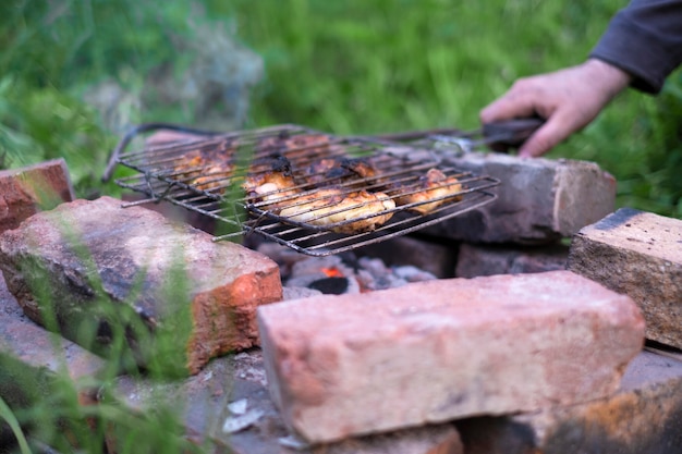 Man cooking meat barbecue on the grill in his garden on simple bricks