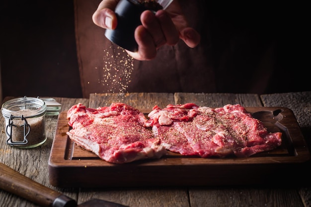 Man cooking meat steaks on kitchen. Chef salt and pepper meat on wooden background