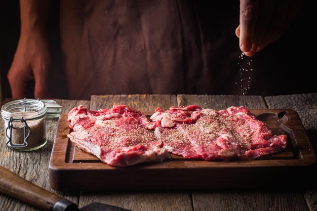 Man cooking meat steaks on kitchen. Chef salt and pepper meat on wooden background