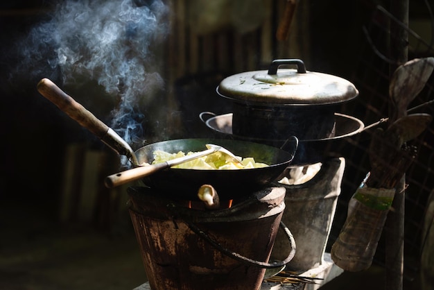 薪ストーブでフライパンで野菜を調理する男は、家で食べるために自分で薪を調理します