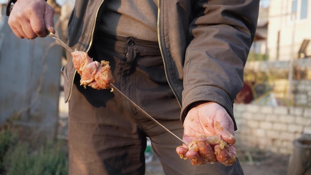 男は通りの炭火焼きで串に刺してバーベキューを調理します 自然の中でバーベキュー アウトドア ピクニック 串に刺した肉を餌にします