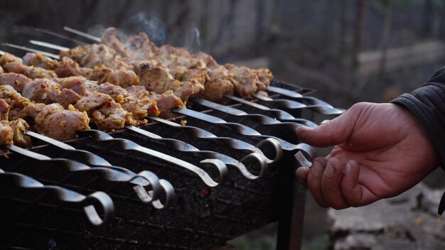 男は通りの炭火焼きで串にバーベキューを調理します 自然の中でバーベキュー屋外ピクニック 焼き肉のクローズアップで串を回転させます