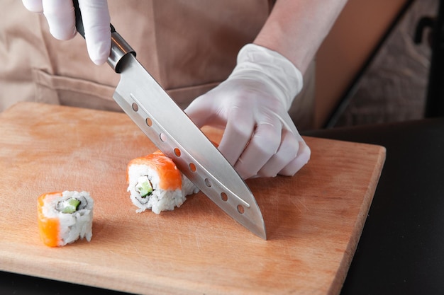 Man cooks sushi on wooden board in gloves for safe cooking