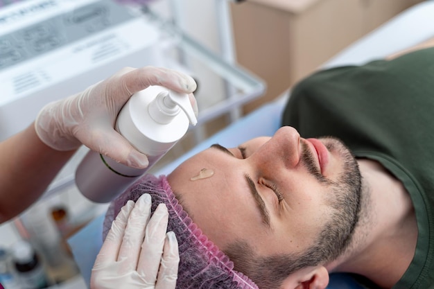 Man at cosmetologist. Relaxing, face closeup, top view. Adjusting cosmetic spray on a forehead. Beauty industry concept. Guy enjoying in cosmetology.