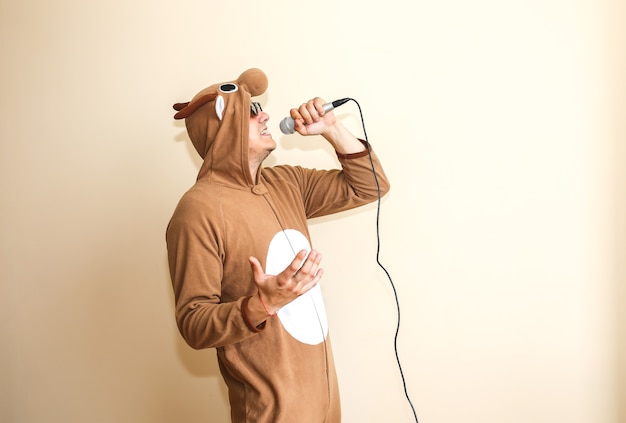 Man in cosplay costume of a cow singing karaoke. Guy in the funny animal pyjamas sleepwear holding microphone. Funny photo with reel tape recorder. Party ideas. Disco retro music.