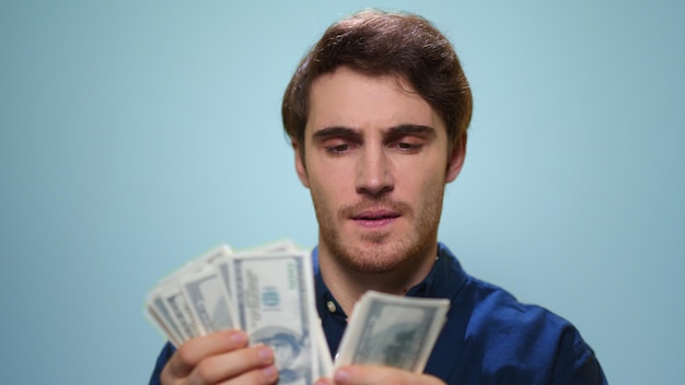 man counting money on blue background satisfied guy holding cash in studio