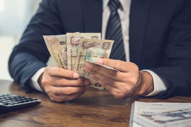 Un uomo che conta soldi, banconote degli emirati arabi uniti dirham, alla sua scrivania