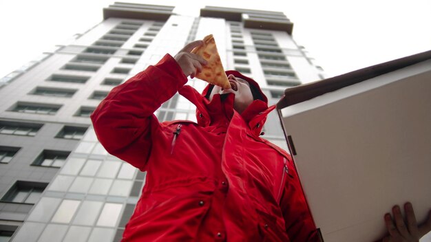 A man courier delivering pizza  takes a piece and bite it