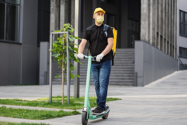 Man courier food delivery with yellow face mask and thermal backpack rides on street