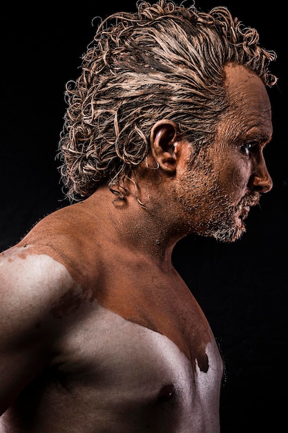 man covered in mud, naked, in profile