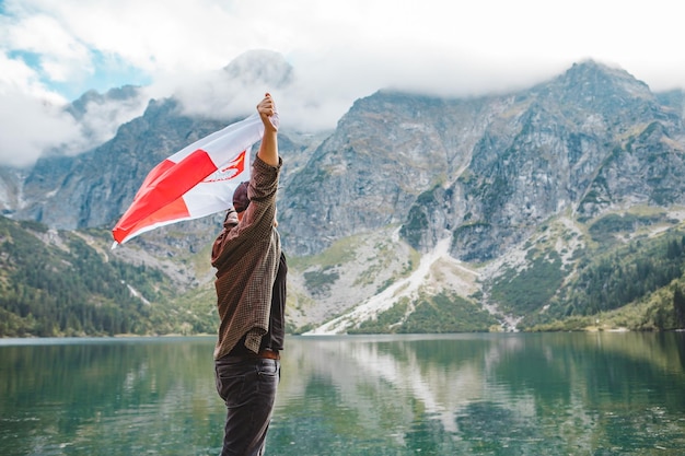 Man covered in poland flag standing on the edge looking at lake in mountains