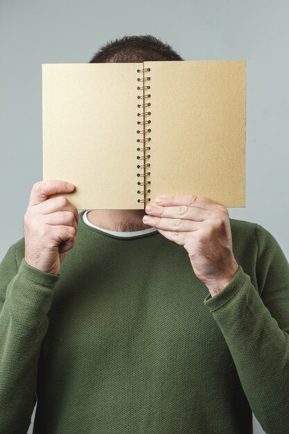 The man covers his face with a notebook.