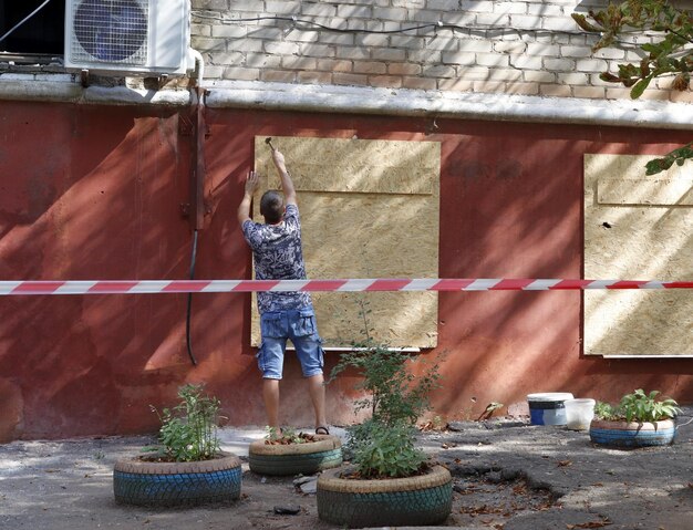 A man covers windows broken after a rocket attack with plywood