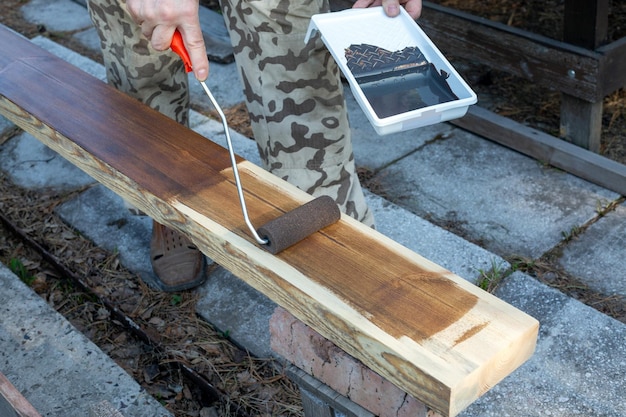 A man covers a wooden board with stain using a roller Hobby carpentry